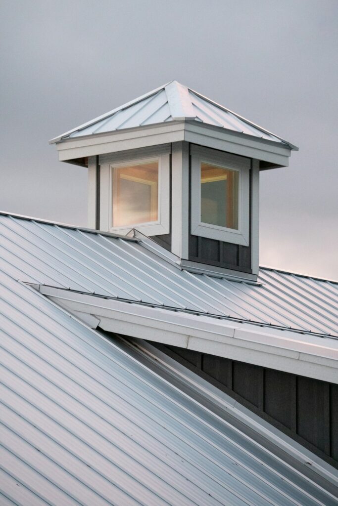 A residential house with one asphalt-shingle roof section and one standing-seam metal roof section under light snow.